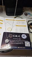 Photo of the moissanite necklace placed on top of the GRA certificate showing the pendant and the chain with good detail on the large central stone and certificate information.