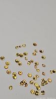 Multiple tiny round diamond cut yellow Ceylon sapphires scattered on a white surface showing color and clarity.