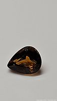 Pear-shaped golden yellow tourmaline gemstone placed on a plain surface showing facets and color.