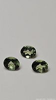 Three mint green, oval cut, faceted apatite gemstones arranged on a plain white background showing facets and color.