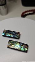 Two rectangular natural abalone shell doublet cabochons with iridescent blue, green, and gold colors on a white background.