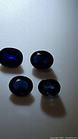 Four deep blue oval cut natural sapphires placed on a white background showing faceted tops and reflecting light.