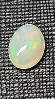 Oval cabochon cut natural Ethiopian opal gemstone placed on black textured background, showing internal play of color.