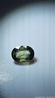 Close-up photo of the oval cut natural green sapphire gemstone under diffused light showing color and clarity details.