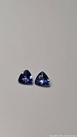 Photo of two trillion cut natural tanzanite gemstones placed side by side on a plain light surface, showing their blue-purple color and clarity.