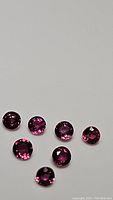 Seven hot pink purple round-cut sapphires on a neutral background, clearly showing their VVS flawless clarity and faceting.