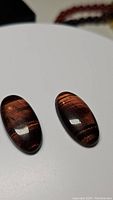 Pair of polished natural red tiger's eye gemstones with vivid chatoyant flash effect on a white background.