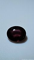 Single oval-shaped deep purple sapphire gemstone displayed on white background showing facets and minor natural inclusions.
