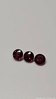 Three natural untreated blood red rubies, round cut, laid out in a row showing size and color consistency under direct light.