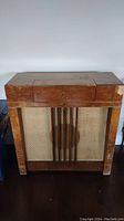 Front view of the wooden antique radio cabinet showing wooden grille with vertical slats and fabric speaker cover.
