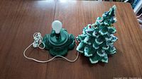 Ceramic Christmas tree parts, base with light bulb socket and electrical cord with bulb on wooden table
