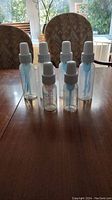 Six Dr. Brown's plastic baby bottles with white caps and vent inserts, standing on a wooden table. Includes four larger bottles and two smaller bottles.