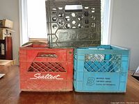 Three milk crates stacked: black Natrel crate on top, red Sealtest crate left bottom, blue Beatrice Foods crate right bottom, showing brand names and crate vent patterns.