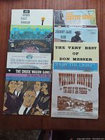 Photo shows 10 country vinyl record album covers laid flat in two columns on a wooden surface. Titles and artists are visible on the covers, mostly vintage country music albums.