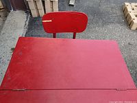 Top view of red school desk showing hinged wooden desktop with some surface wear