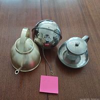 Set of two metal tea pots and one spherical metal tea steeper with chain on wooden table