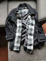 Photo of folded black woman's coat with checkered lining showing.