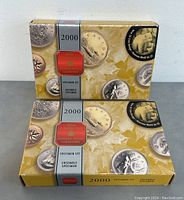 Two original retail boxes of the 2000 Royal Canadian Mint specimen proof sets shown stacked with coins decoration and maple leaf background