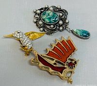 Three vintage brooches displayed on a grey background showing front detail.