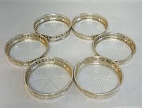 Six Birks sterling silver rimmed crystal coasters arranged on white background looking down from above showing complete set and detail of crystal bases.
