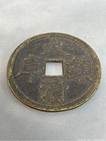Top view of bronze Feng Shui Chinese coin showing raised Chinese characters around square center hole on one side.