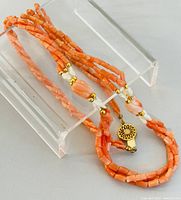 Necklace displayed on a clear acrylic stand showing multiple strands of varied coral beads, freshwater pearls, gold-tone spacer beads and decorative clasp.