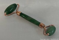 Photo of natural aventurine jade crystal face massage wheel showing larger roller end and part of the jade handle with rose gold metal fittings.