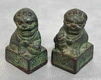 Front view of both bronze Foo Dogs highlighting facial details and base decoration.