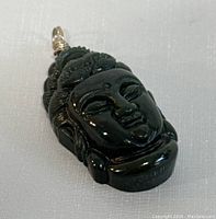 Top view of the deep green jade Buddha pendant showing carved facial details and metal loop
