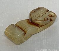 Close-up angled view of carved jade pendant showing front design with engraved traditional Chinese motifs and natural inclusions.