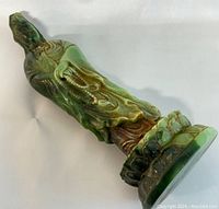 Photo showing side angle view of green jade Kwan-yin statue highlighting color variations and bead details.