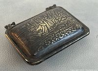 Top and angle views of the small metal pocket box case showing embossed Chinese design and hinge clasp.