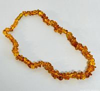 Full view of amber necklace laid flat showing translucent amber beads in varying warm shades and irregular shapes.