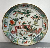 Front view of the round Famille Rose porcelain dish showing detailed decoration of phoenix, dragon, flowers, and garden motifs with vibrant enamels on white background and gold rim.