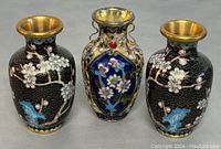 Photo showing all three cloisonne vases, two black cherry blossom vases and one blue floral vase with decorative handles.