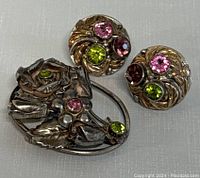 Front view of vintage sterling silver floral brooch and two matching round crystal clip-on earrings with pink, green, and purple stones.