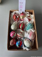 Box with 12 glass Christmas ornaments of varying shapes and colors packed with tissue paper.