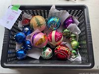Photo of basket containing 16 round vintage glass Christmas ornaments in various colors and sizes with visible hand-painted holiday designs.