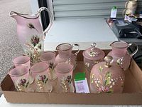 Complete view of the antique hand-painted frosted glass drink set with pitcher, glasses, smaller pitchers, sugar jar, and covered dish in a cardboard tray.