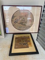 Frontal view of two Asian art pieces: the framed circular silk artwork with horsemen and a framed black matboard holding two square metal animal panels.