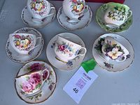 Seven sets of decorative teacups and saucers arranged displaying floral patterns