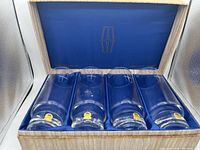 Set of four clear lead crystal glasses with thick bases and etched designs in a blue fabric-lined box.