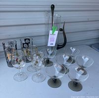 Wide shot showing full mid century glassware cocktail set including pitcher, stir stick, six stemmed glasses, three bubble glasses with gold accents, and two geometric banded highball glasses.