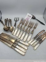 Full view of flatware set showing mother of pearl handles with silver and sterling bands, knives, forks, spoons, and serving forks.