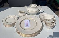 Wide view showing the stacked dinner plates, tea plates, cups, saucers, creamer, and teapot all arranged on a table under sunlight