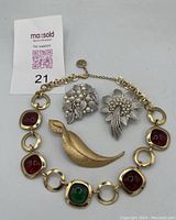 Full lot of four Trifari signed jewelry pieces including two floral rhinestone and faux pearl brooches, one gold-tone leaf brooch, and one gold-tone bracelet with red and green stones.