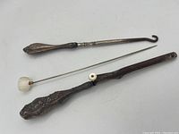 Photo showing the full set of Victorian vanity items: glove stretcher, shoe button hook, and hat pin aligned horizontally on a white background.