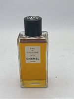 Front view of vintage Chanel No. 5 Eau de Cologne 4-inch bottle with amber-colored perfume and black cap with white Chanel logo.