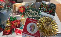 Box with various vintage Christmas decorations including atomic foil balls, garlands, poinsettia flowers, Merry Christmas sign and boxed chandelier lights.