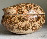 Close-up photo of large egg-shaped clay roaster lid showing detailed fall leaf pattern glazing